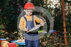 Little boy child future engineer builder architect with safety helmet with drawing, looking on new buildings and