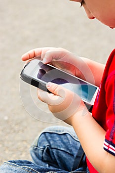 Little boy child playing games on mobile phone outdoor