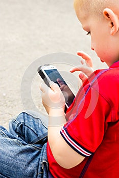 Little boy child playing games on mobile phone outdoor