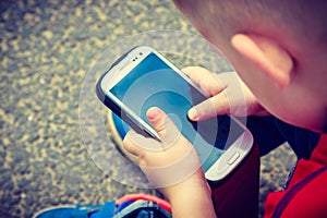 Little boy child playing games on mobile phone outdoor