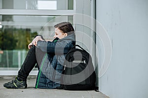 Little boy or child sitting alone on floor in front of the school after suffering an act of bullying