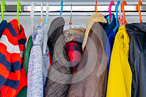 Little boy child size jackets, coats and sweaters hanging in a kid`s closet with colorful hangers photo