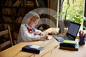 Little boy child studying at home table sitting front of computer laptop