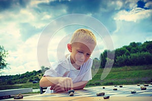 Little boy clever child playing checkers in park