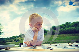 Little boy clever child playing checkers in park