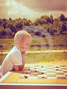 Little boy clever child playing checkers in park