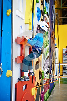 Little boy is climbing in child sport park on blue wall