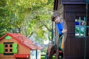 Little boy climbing ladder on slide at playground. Child is 5 7 year age. Caucasian, casual dressed in jeans and pullover.