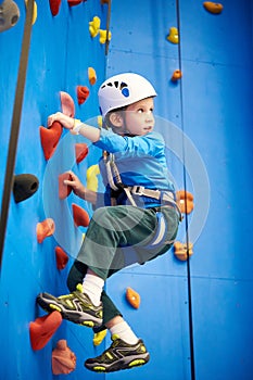 Little boy is climbing in sport park on blue wall