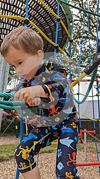 A little boy climbing up a rope ladder on a playground climbing frame