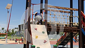 A little boy climbs a children`s slide for mountaineering. The child plays on the playground.