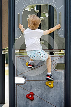 A little boy climbs up a climbing wall on an outdoor playground