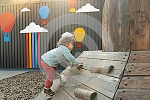 Little boy climbs the wooden slide in the playground outdoors