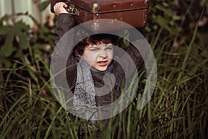 A little boy in a coat sneaks through the tall grass, with a suitcase on his head.