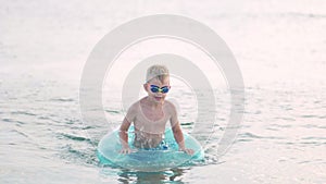 Little boy comes out of the sea ocean water, child having fun, swimming on blue swimming ring. Summer vacation, holiday