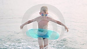 Little boy comes out of the sea ocean water, child having fun, swimming on blue swimming ring. Summer vacation, holiday