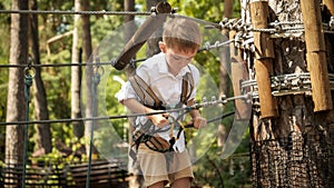 Little boy connecting his safety rope and hook before climbing up the tree in park