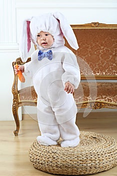 Little boy in costume bunny standing on pouf with photo