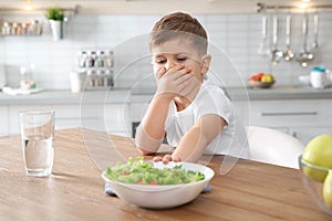 Little boy covering his mouth and refusing to eat vegetable salad at table