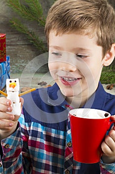little boy with a cup of hot chocolate with marshmallows and snowman on the background of gifts, Christmas tree and Christmas de