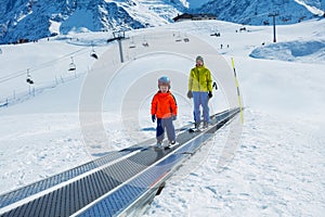 Little boy and a dad go up on the ski moving walkway