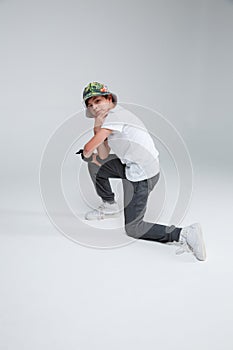 A little boy is a dancer breakdance dancer, sitting in the knee holding his hand near the chin.