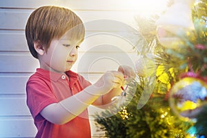 Little boy decorating Christmas tree with toy balls