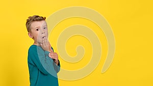 A little boy demonstrates the emotion of fright or surprise, half covering his mouth with his hand. White isolated background.