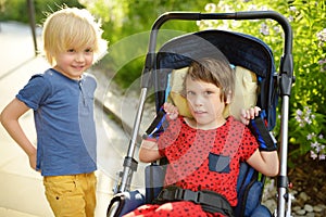 Little boy and disabled girl in wheelchair playing together in summer park. Child cerebral palsy. Family with disabled kid.