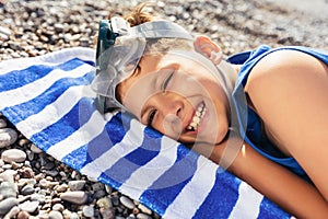 The little boy in diving goggles lying on a Striped blue and white beach towel and smiling