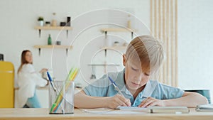 Little boy is doing homework at home sitting at the table, writing in notebook