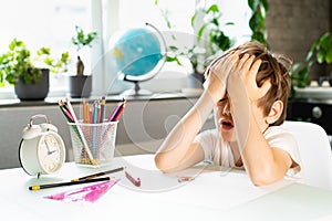 Little boy doing homework at home at the table, overwork of a first-grader from studying, stress of a schoolboy