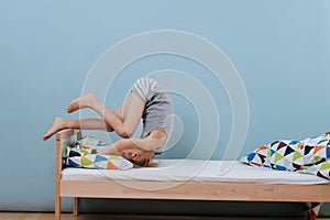 Little boy doing morning gymnastics in unmade bed. Forward roll exercise