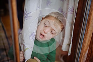 Little boy with Down syndrome looking through window at home.