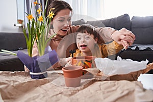 Little boy with down syndrome planting flowers in a brown flowerpots with his mother