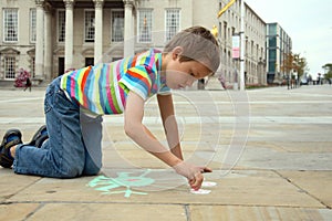 Little boy drawing with chalks on pavement