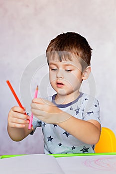 Little boy is holding color pencils. Boy, drawing a picture for fathers day. Small boy draws at the table