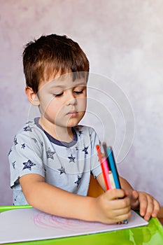 Little boy drawing with color pencils. There are many colored pencils in the boy`s hands. Small boy draws at the table