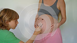A little boy drawing a smiling face on his pregnant mother's belly. The scene exudes warmth and tenderness
