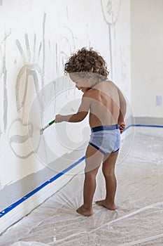 Little boy drawing on a white wall with a paintbrush during home renovations
