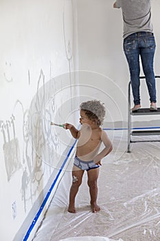 Little boy drawing on a white wall with a paintbrush during home renovations