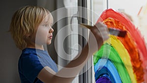 Little boy drawing on window rainbow while coronavirus quarantine. Rainbow sign is symbol of hope