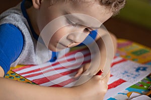 Little boy draws a USA flag. The boy colors the flag with crayons. Education, the study of state symbols, a photo