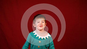 Little boy dressed in an elf shirt acts silly in front of the camera, jumping up and down