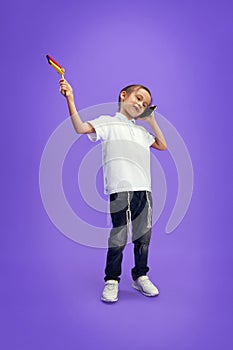 Little boy dressed modern casual outfit playing with grogger toy and talking on phone against purple studio background.