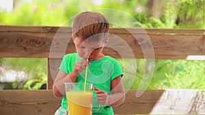 The little boy is drinking fresh orange juice with a straw
