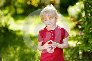 Little boy drinking glass of water in hot sunny summer day on the backyard or home garden