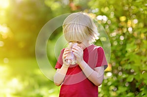 Little boy drinking glass of water in hot sunny summer day on the backyard or home garden