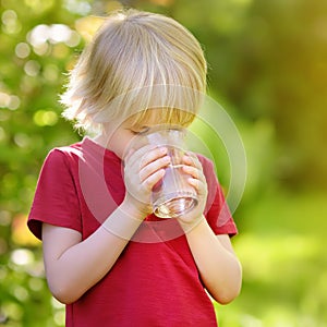 Little boy drinking glass of water in hot sunny summer day on the backyard or home garden