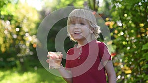 Little boy drinking glass of water on hot sunny summer day in the backyard or home garden. Feeling of thirst.
